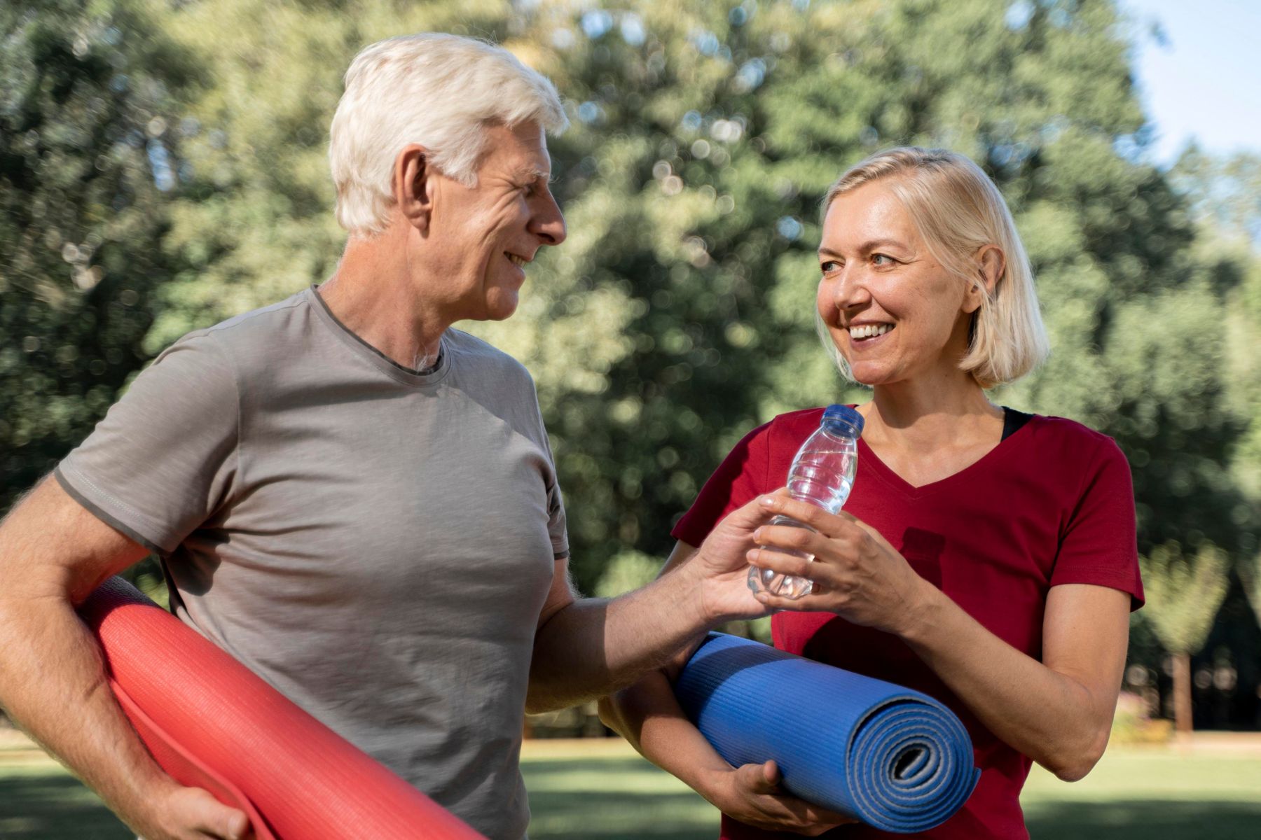 An older couple outdoors with exercise mats, smiling at each other